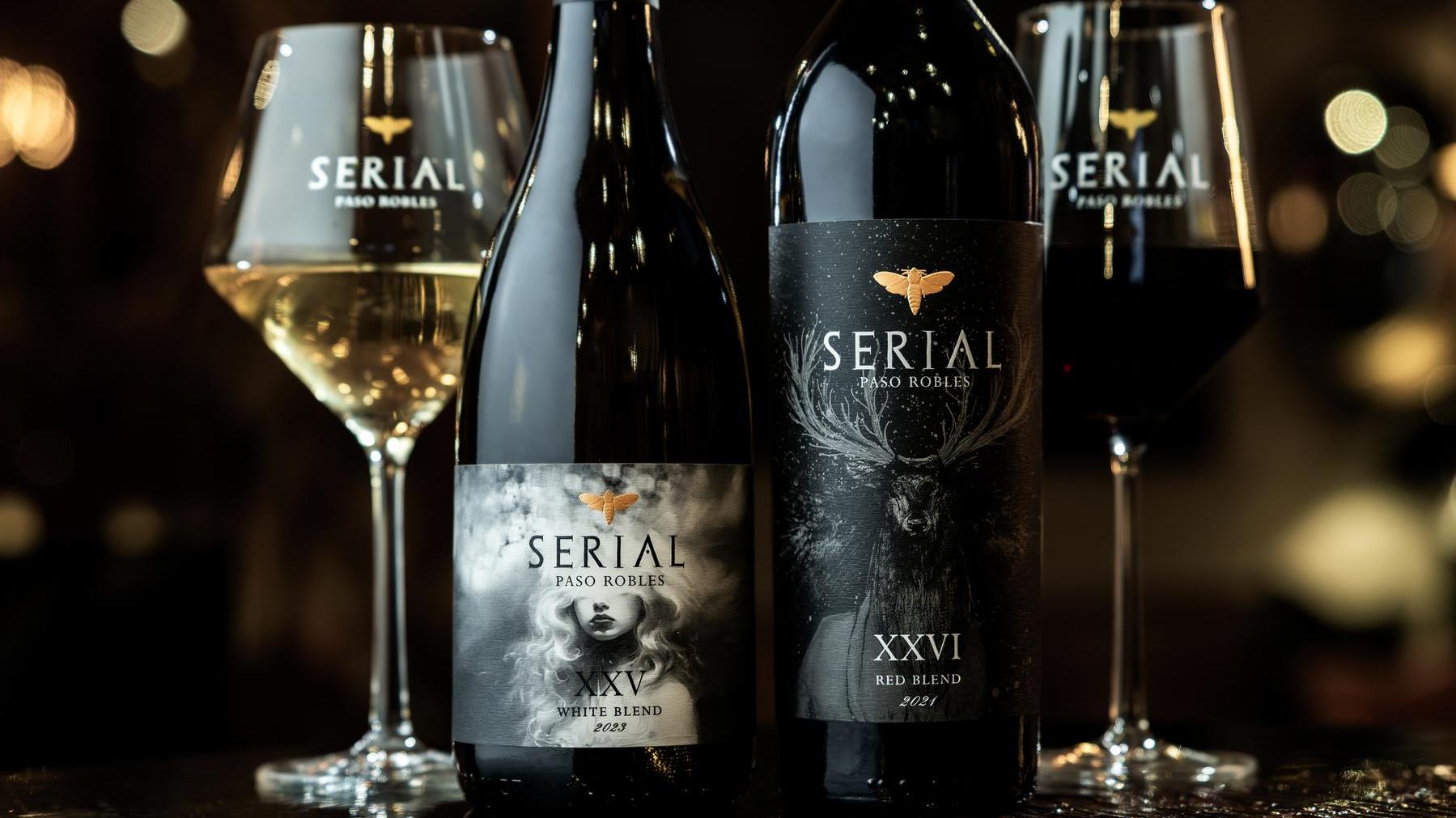 A photo showcasing two bottles of Serial Wines with labels featuring artistic designs. The bottle on the left, labeled Serial White Blend, depicts a young woman in a foggy landscape. The bottle on the right, labeled Serial Red Blend, features a majestic stag standing in the rain. Both bottles are placed in the stunning Serial Wines Tasting Lounge in Paso Robles.